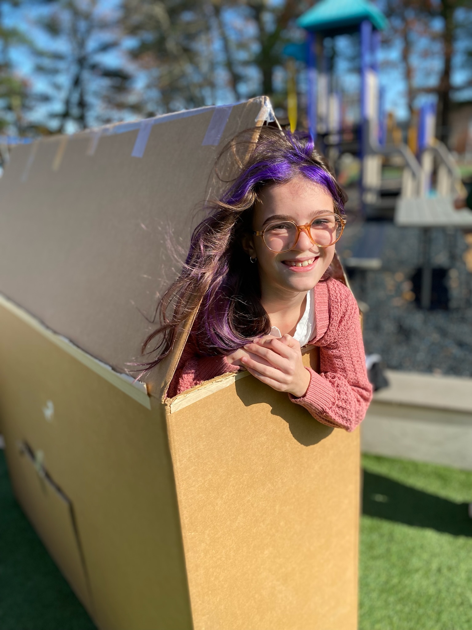 Girl peeking out of a cardboard box creation at the playground